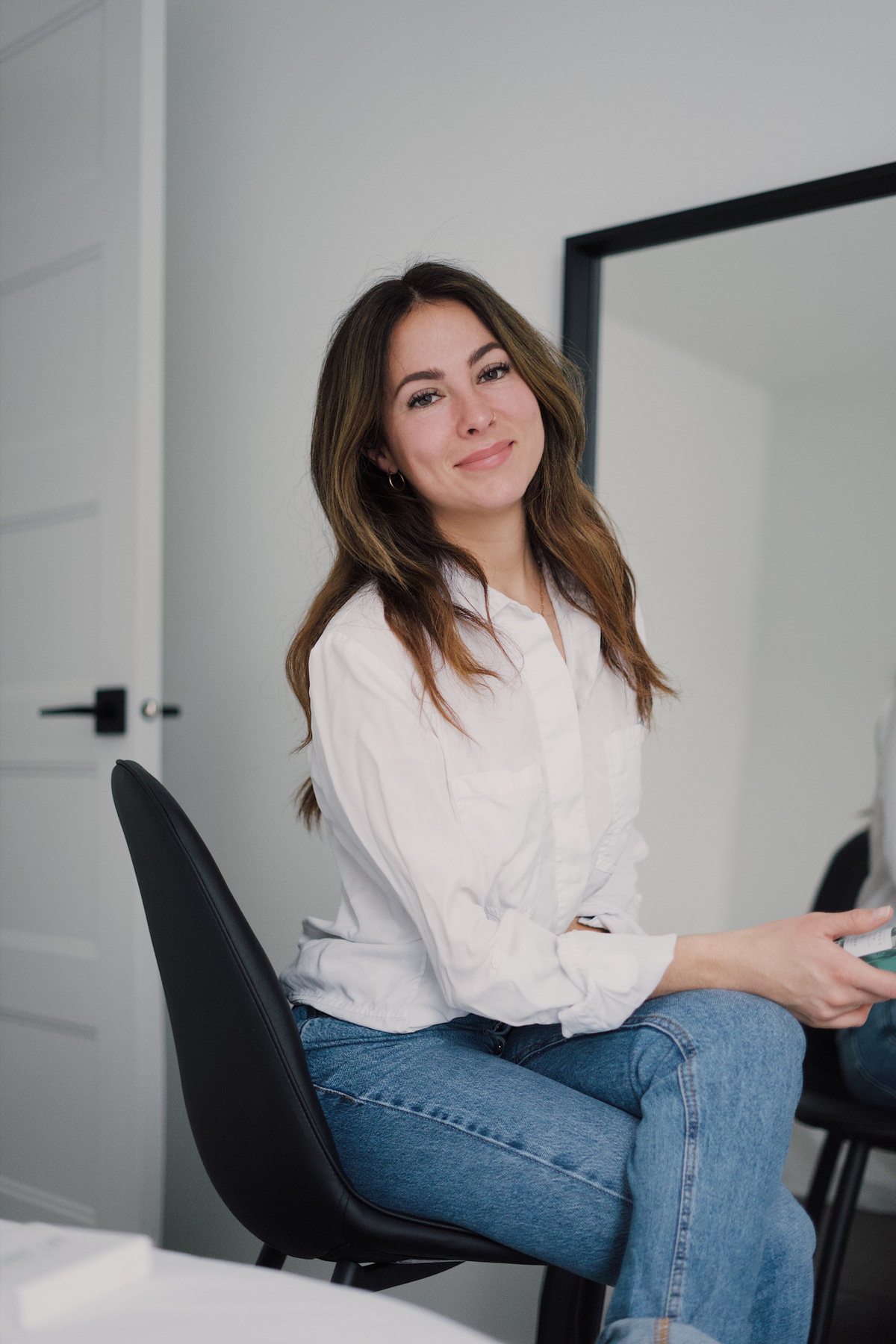 Woman in White Dress Shirt and Blue Denim Jeans Sitting on Black Chair